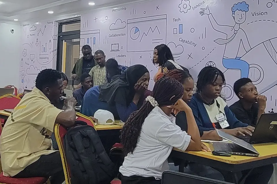 Learners work at laptops around shared tables during a training session.