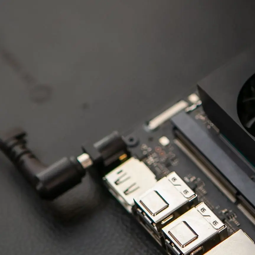 A compact edge AI compute board with its ports and power cable connected, on a dark desk.